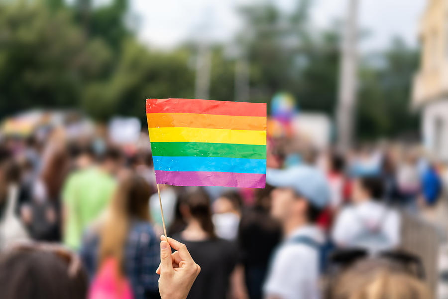 Gay rainbow flag at gay pride parade with blurred participants in the background Photograph by Stock-eye