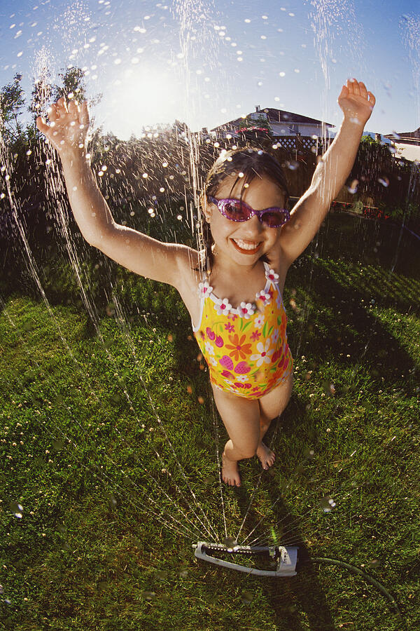 Gel Effect Shot of a Young Girl Wearing a Swimming Costume, Being Sprayed with Water From a Garden Sprinkler Photograph by Darryl Leniuk