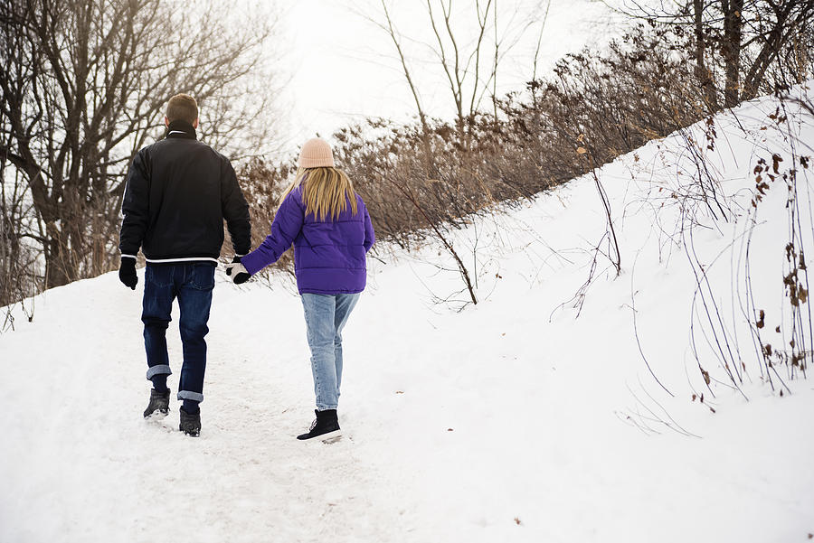 Generation Z couple walking in snowy public park trail in winter. Photograph by Martinedoucet