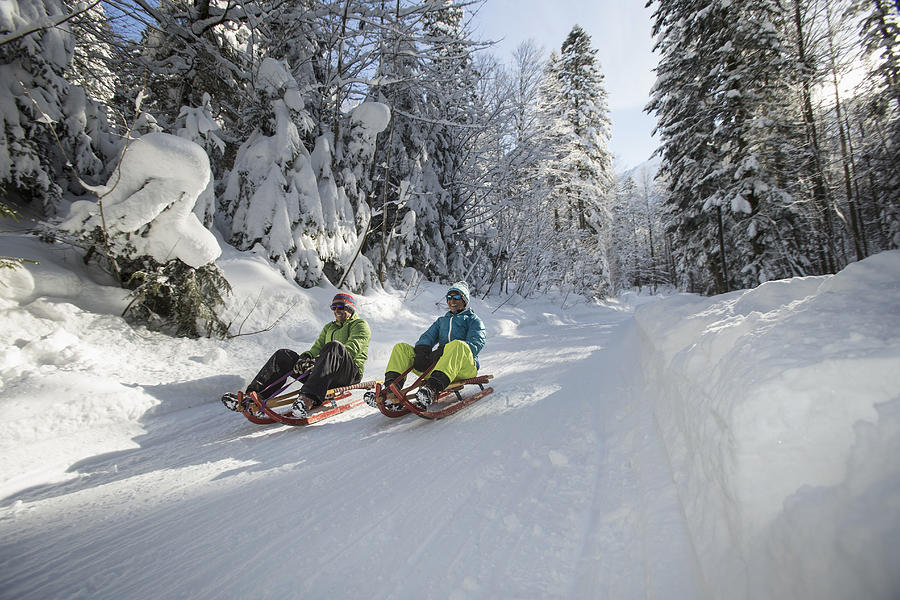 Germany, Bavaria, Inzell, couple having fun on sledges in snow-covered landscape Photograph by Westend61