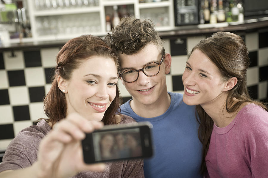 Germany, Bavaria, Munich, Young friends taking photo with mobile phone in cafe Photograph by Westend61