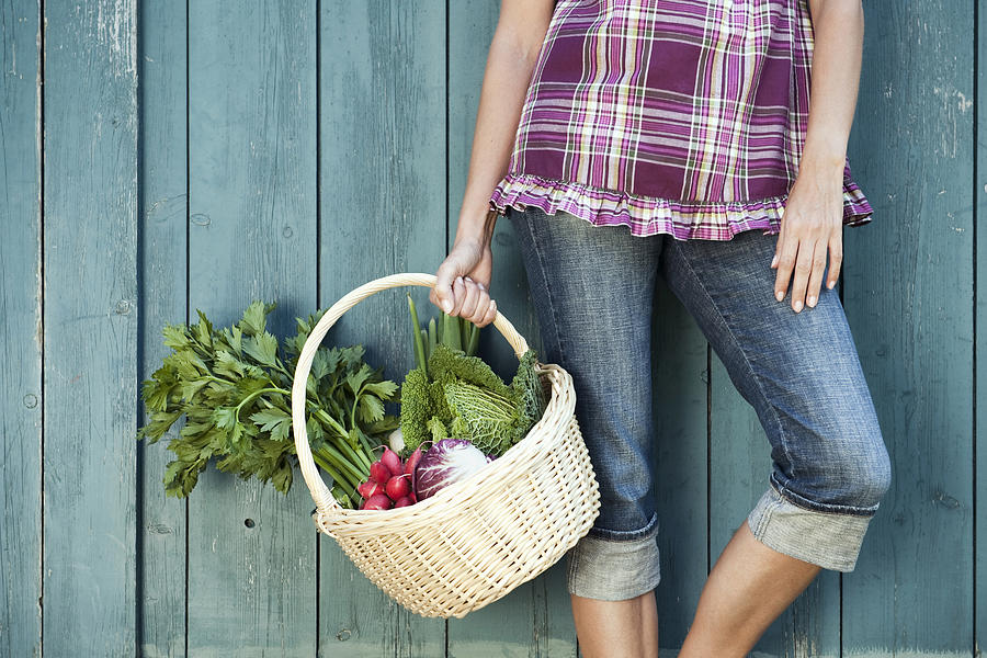 Germany, Bavaria, Woman leaning against barn door holding basket with fresh vegetables Photograph by Westend61