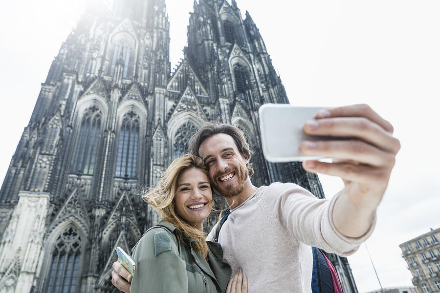 Germany, Cologne, portrait of young couple taking a selfie in front of Cologne Cathedral Photograph by Westend61