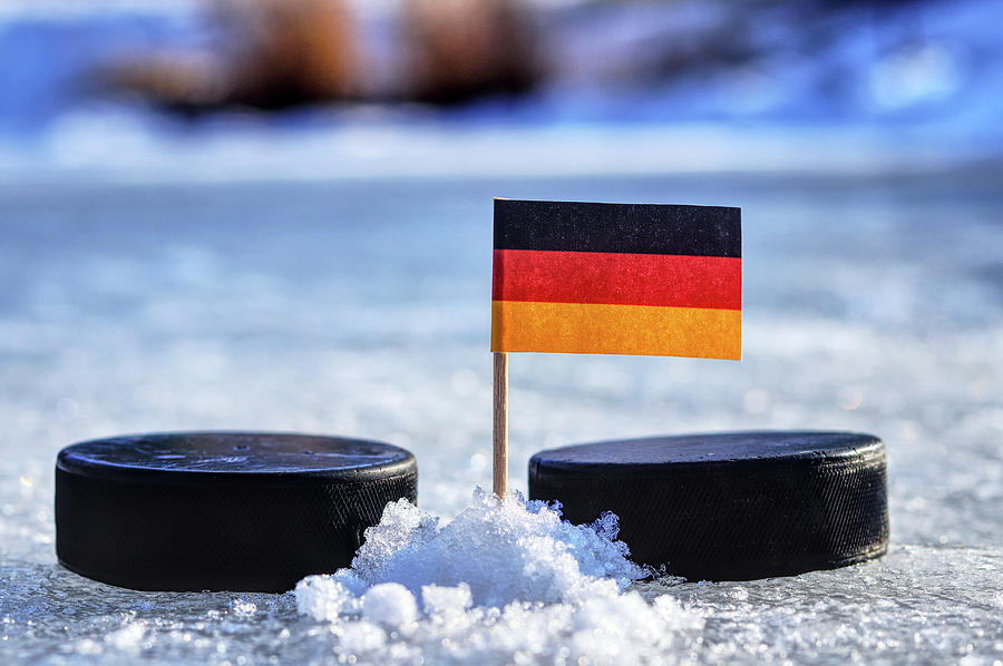Germany flag on toothpick between two hockey pucks. Winter classic. Flag on frozen pond on unkempt ice. Traditional pucks for international matches. Photograph by Vaclav Sonnek
