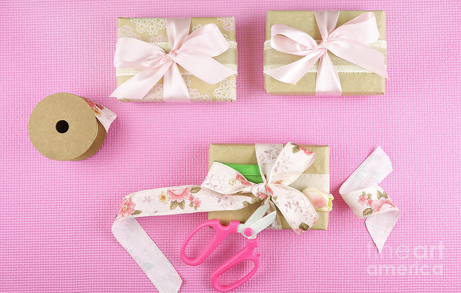 Gifts wrapped in kraft paper and pink ribbons overhead flatlay. Photograph by Milleflore Images