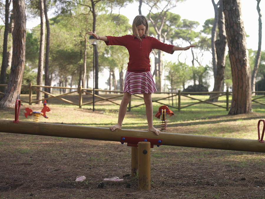 Girl (10-12) balancing atop seesaw, arms outstretched Photograph by Ascent/PKS Media Inc.