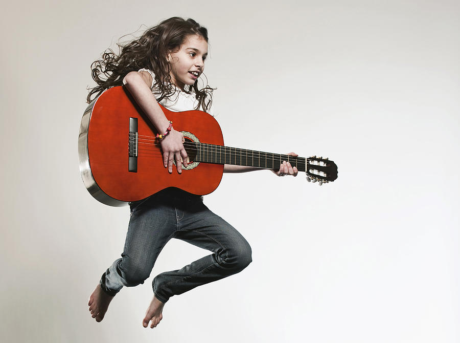 Girl (12-13) playing guitar and jumping Photograph by Westend61