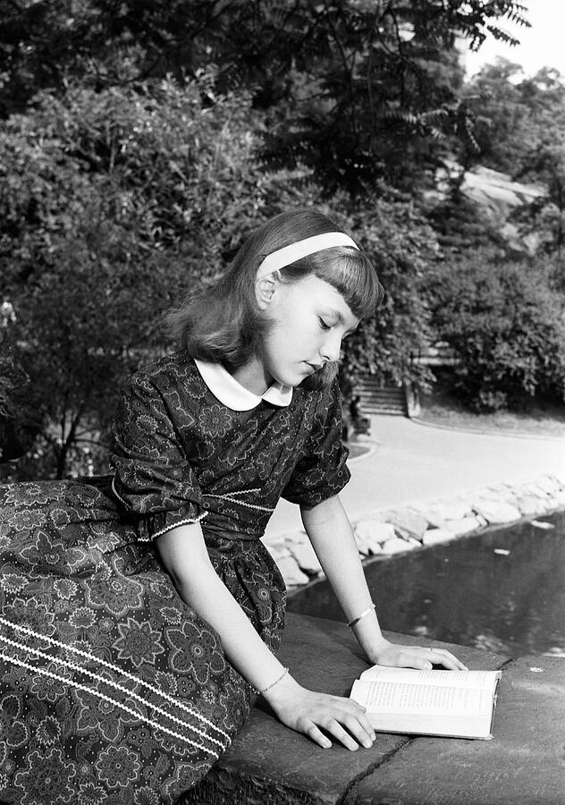 Girl (12-13) reading book, sitting on bridge in park Photograph by George Marks