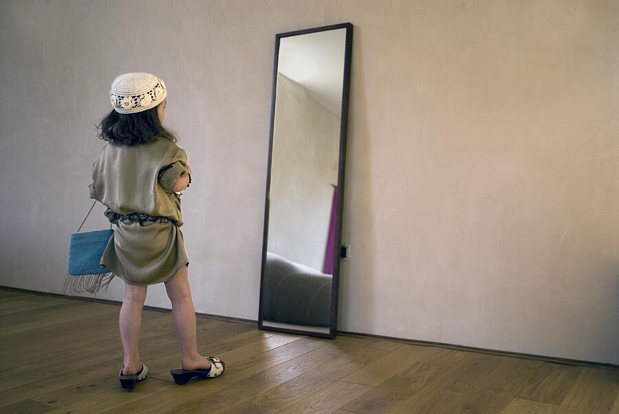 Girl (2-4 years) dressing up for party, posing in mirror. Photograph by Luc Beziat