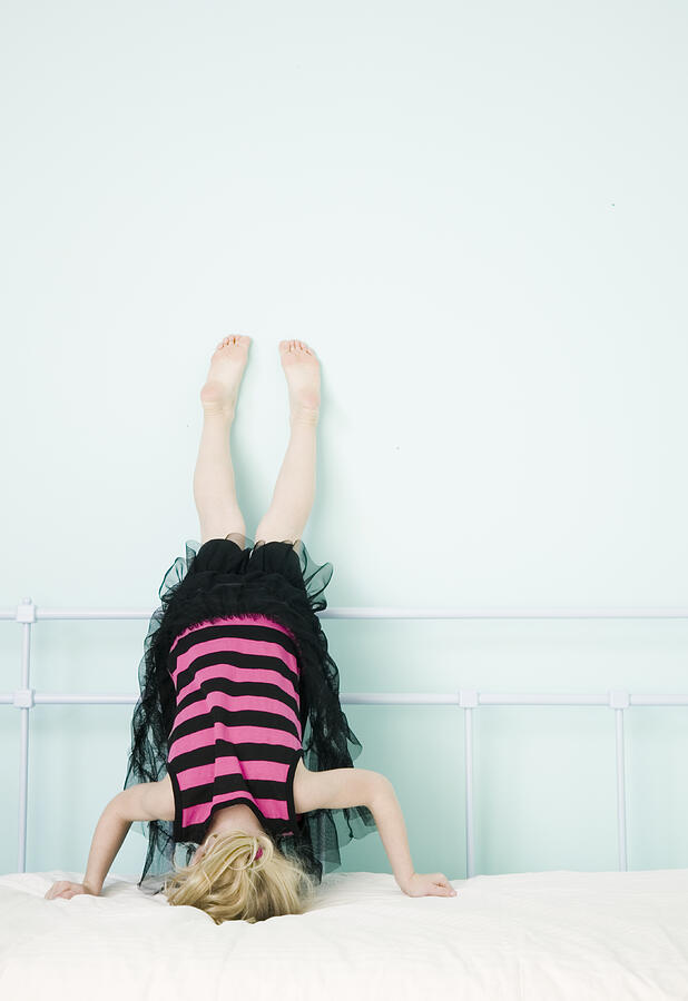 Girl (3-5) doing handstand against wall on bed Photograph by Steve Wisbauer