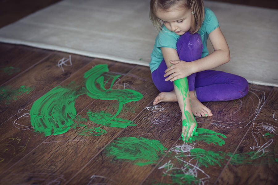 Girl (4-5) smearing green paint on herself and living room floor Photograph by Elva Etienne