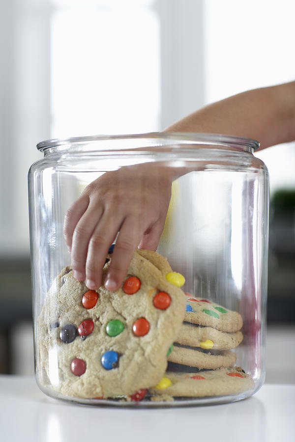Girl (4-6) reaching into cookie jar, close-up Photograph by Thomas Northcut