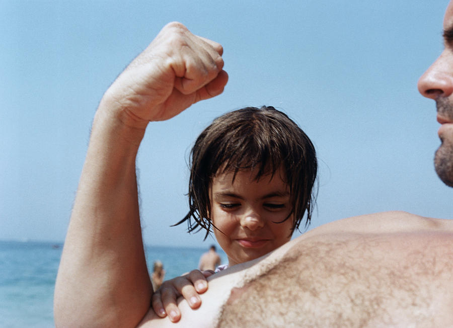 Girl (5-7) feeling fathers muscles on beach, close-up Photograph by Mario Lalich