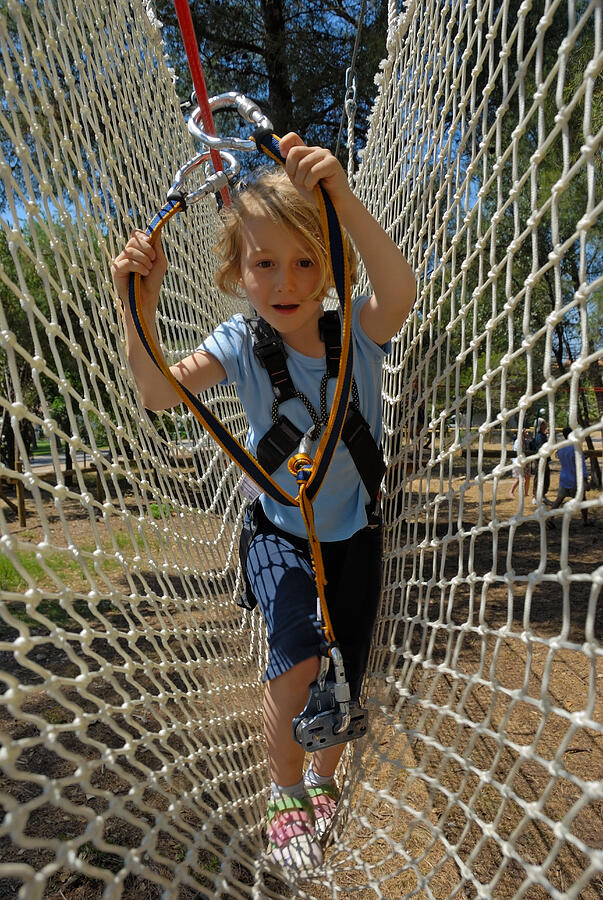 Girl (5-7), holding rope, crossing netting in adventure playground Photograph by Sami Sarkis