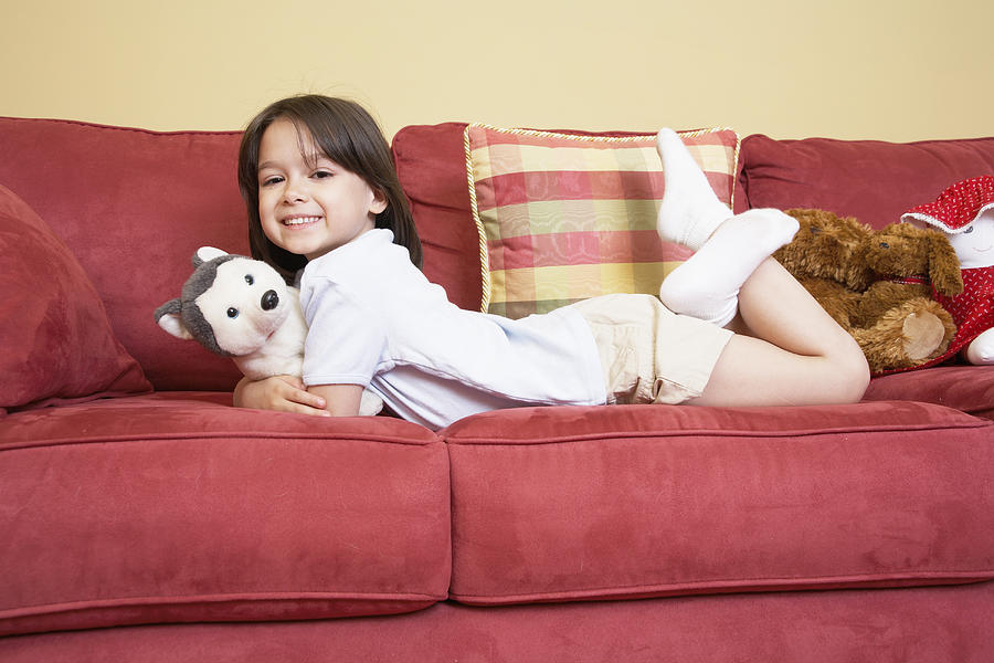 Girl (5-7) lying on sofa with stuffed animals, portrait Photograph by DCA Productions