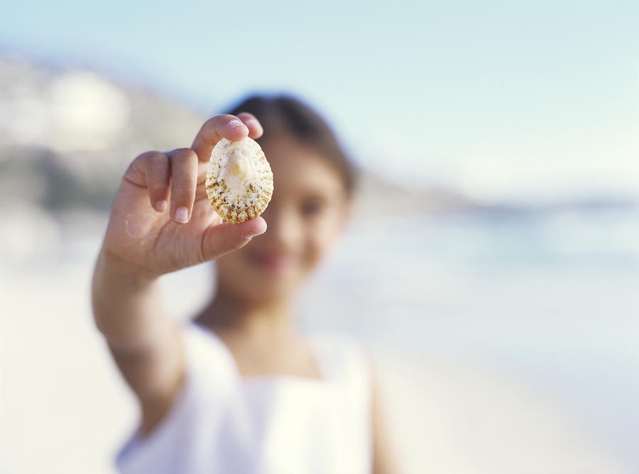 Girl (5-7) on beach holding shell, close up, portrait Photograph by Ciaran Griffin