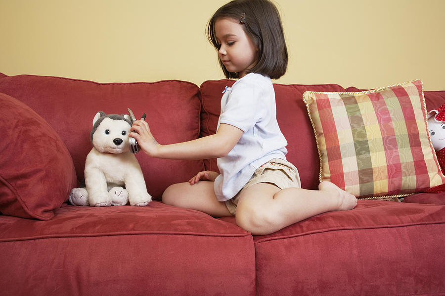 Girl (5-7) playing with stuffed animal on sofa Photograph by DCA Productions