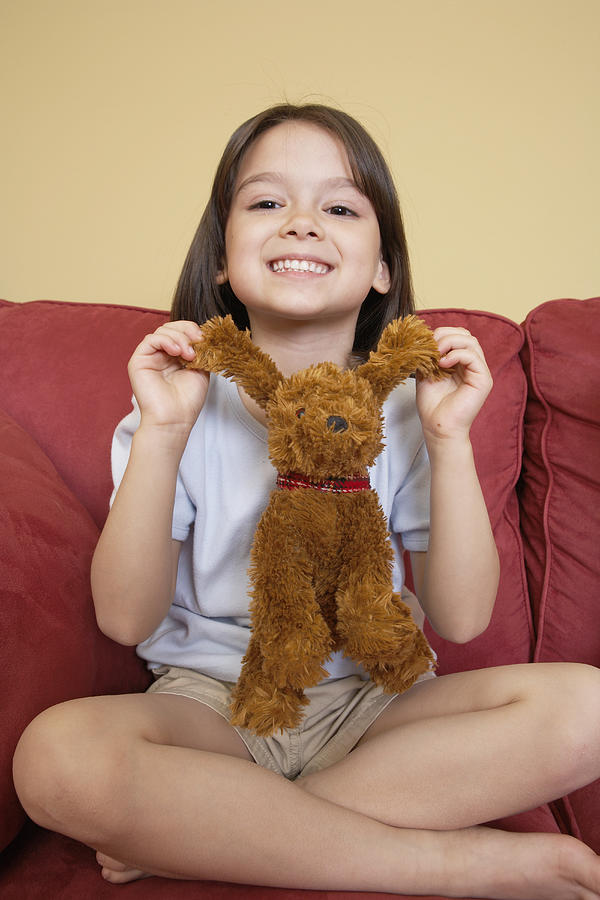Girl (5-7) sitting on sofa with stuffed animal, portrait Photograph by DCA Productions