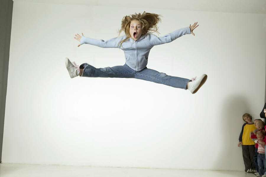 Girl (6-7), jumping with arms and legs outstretched, on trampoline in studio, portrait Photograph by Photodisc