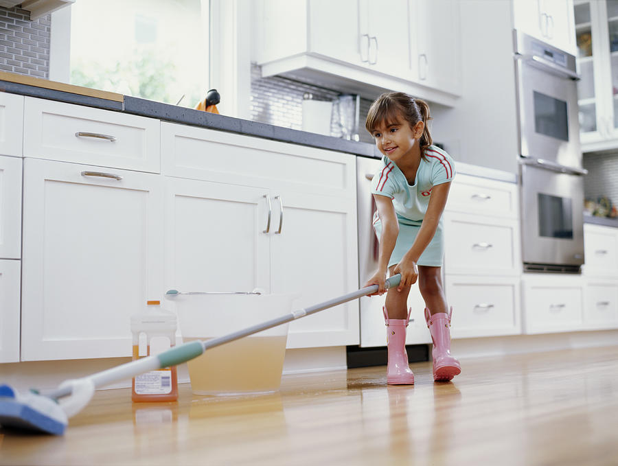 Girl (6-8) cleaning kitchen floor with mop, smiling, low angle view Photograph by Kraig Scarbinsky