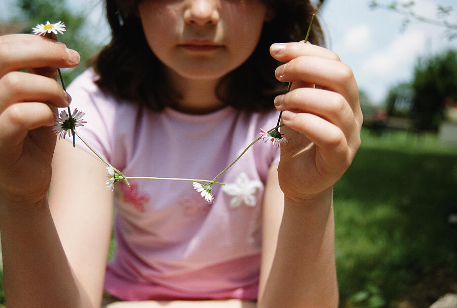 Girl (7-9) holding up daisy chain, close-up Photograph by Stuart Paton