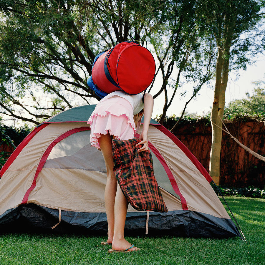 Girl (8-10) holding bags, bending over by opening of tent, rear view Photograph by Clarissa Leahy