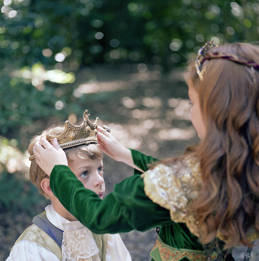 Girl (8-10) in costume putting crown on boys head Photograph by Siri Stafford
