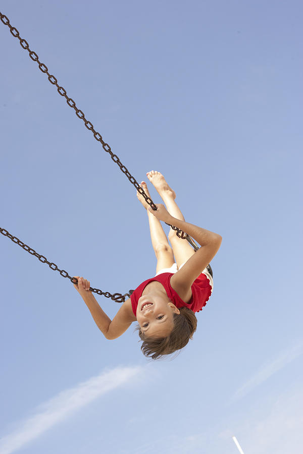 Girl (8-10) playing on swing, swinging upside down, portrait Photograph by Christopher Robbins