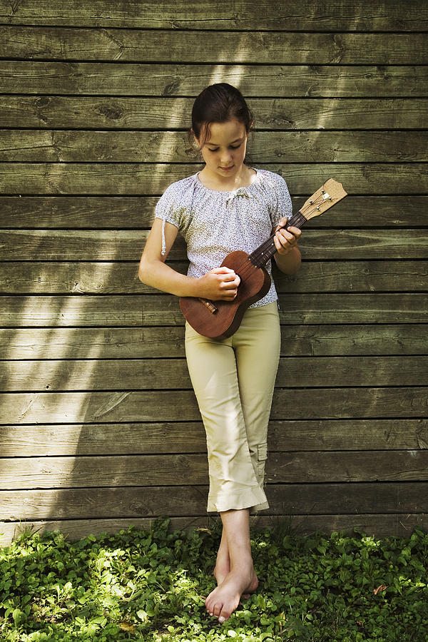 Girl (8-9) leaning against fence, playing ukulele Photograph by Ron Levine