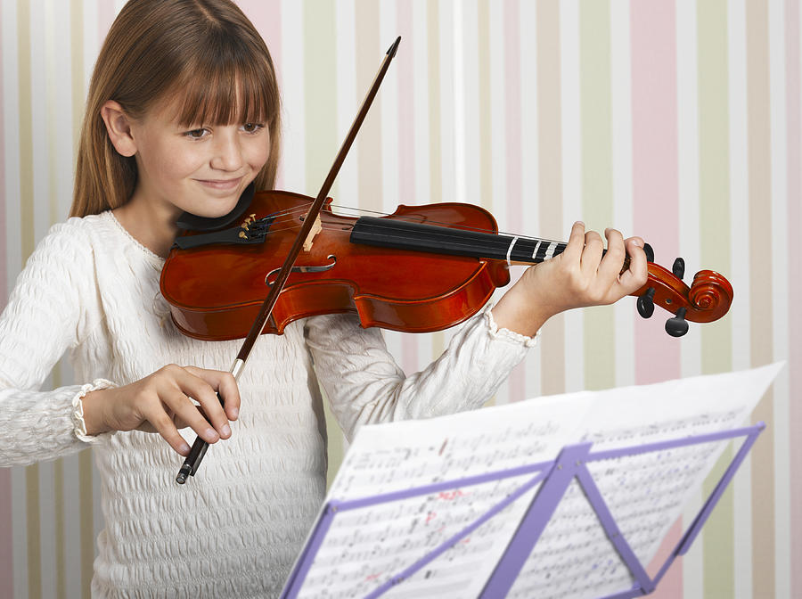 Girl (8-9) playing violin, smiling Photograph by Peter Dazeley