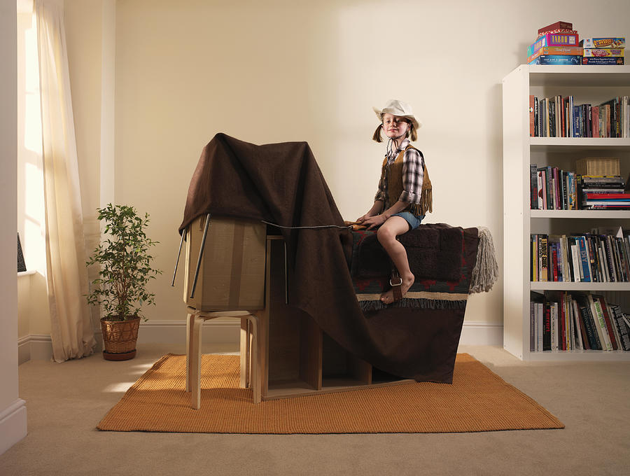 Girl (8-9) pretending to ride horse made from furniture and blanket Photograph by Tim Macpherson