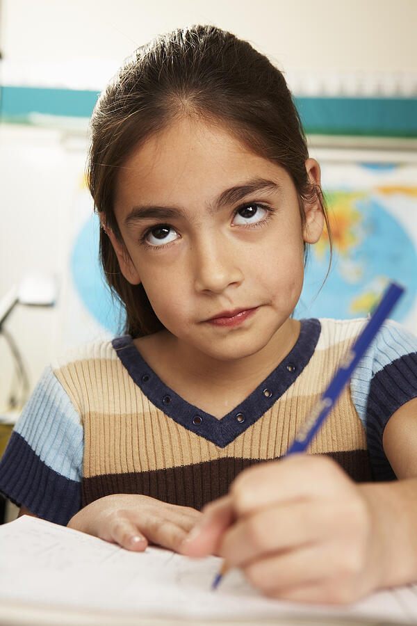 Girl (8-9) sitting and writing at desk in classroom, close-up, portrait Photograph by Yellow Dog Productions