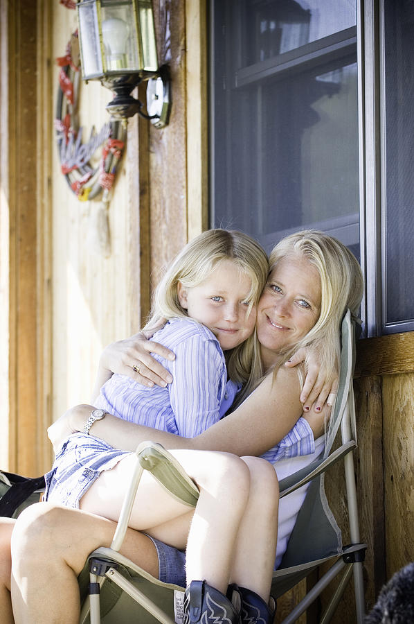 Girl (9-11) snuggling in mothers lap on porch, portrait Photograph by Stephen Simpson