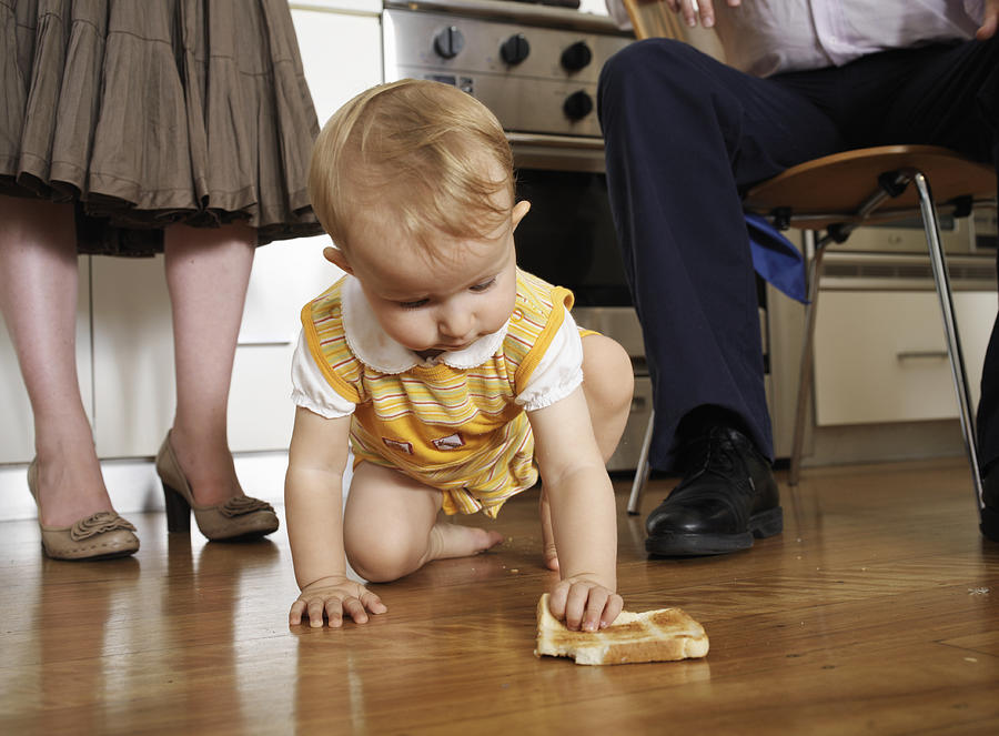 Girl (9-12 months) crawling on floor in kitchen with parents, low section Photograph by David Woolley