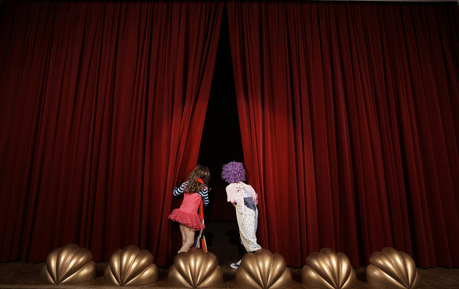 Girl and boy (5-7) on stage, looking through curtains, rear view Photograph by Adam Taylor