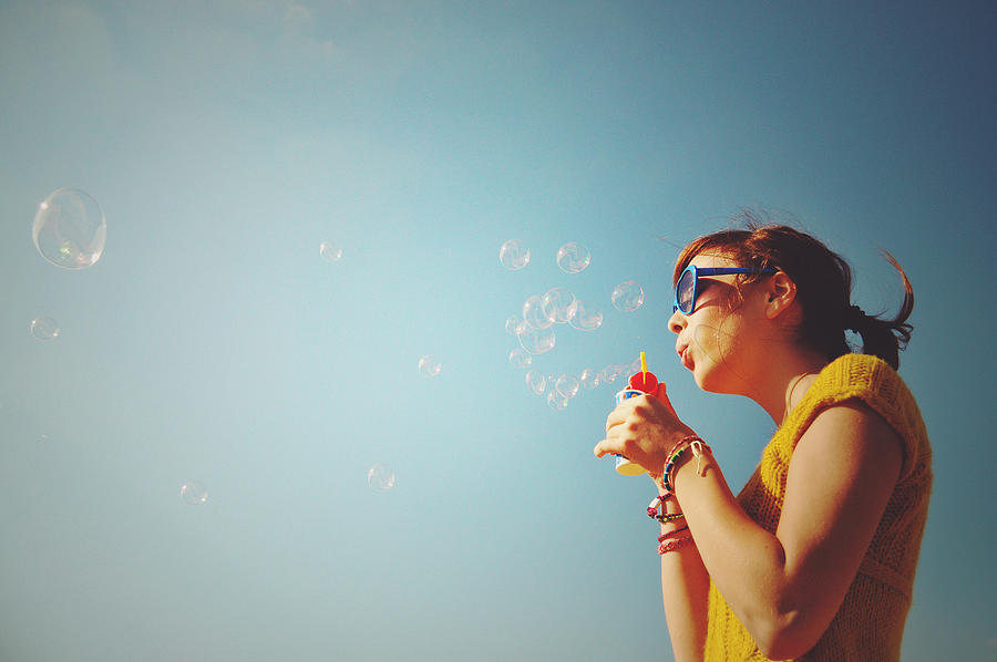 Girl blowing bubbles into blue sky Photograph by Marie Frenzel