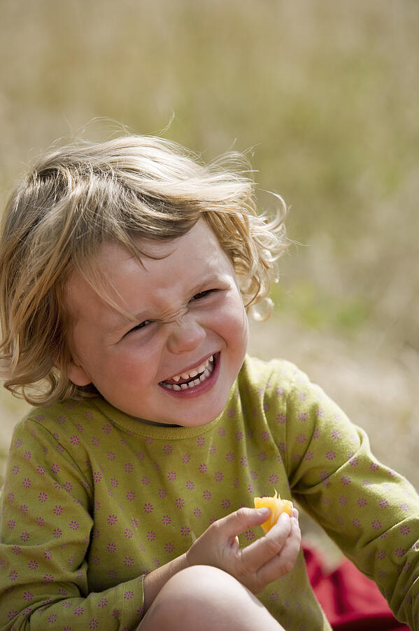Girl eating fruit and laughing Photograph by Comstock Images