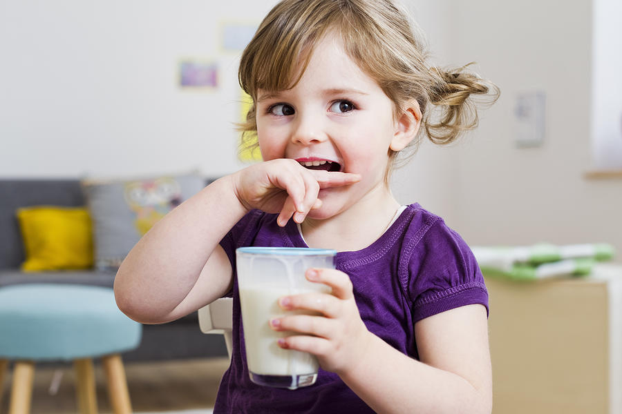 Girl holding glass of milk at home Photograph by Emely
