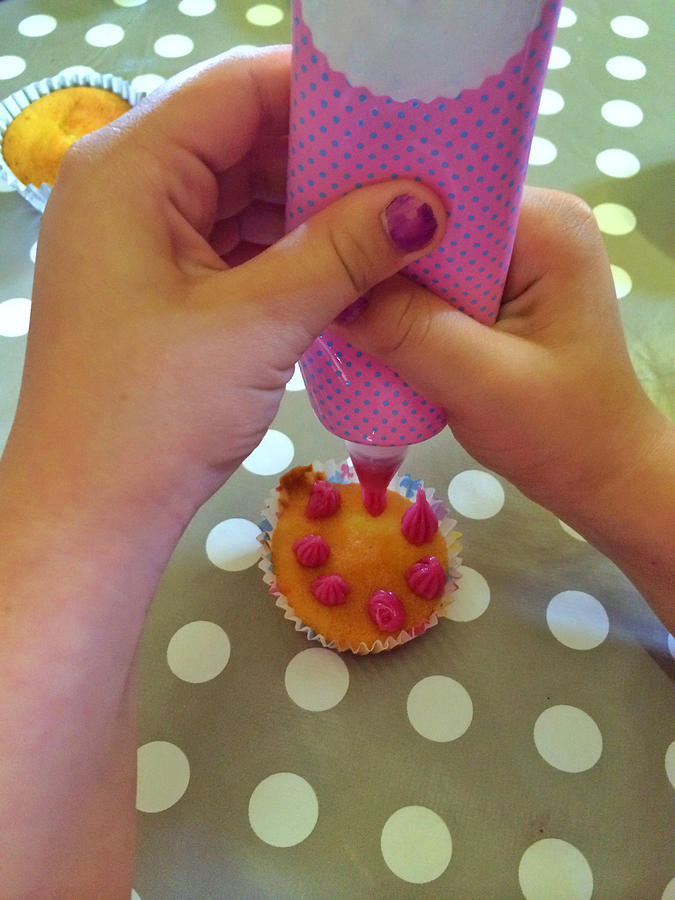 Girl icing a cupcake in kitchen Photograph by Snapper