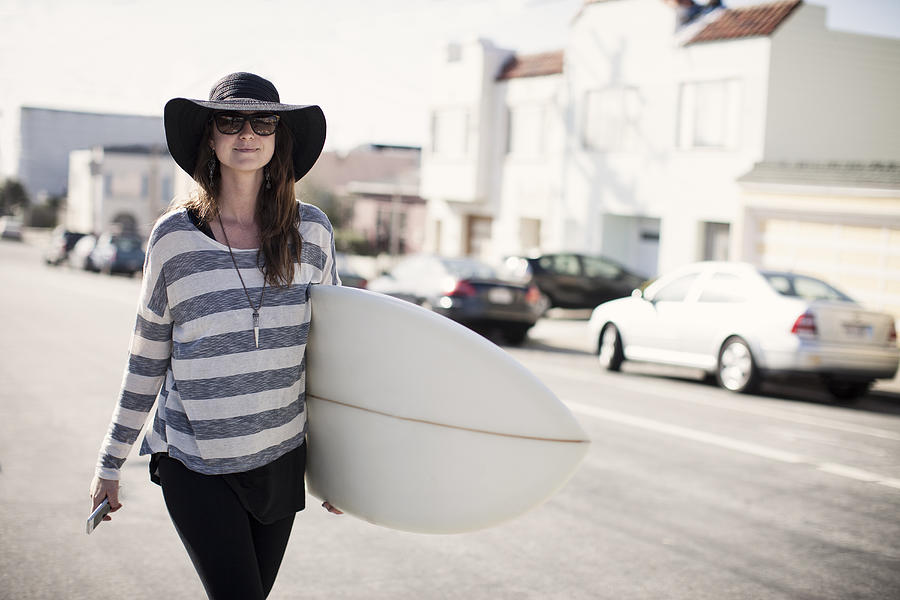 Girl in black hat walking w/surfboard & cell phone Photograph by Justin Lewis