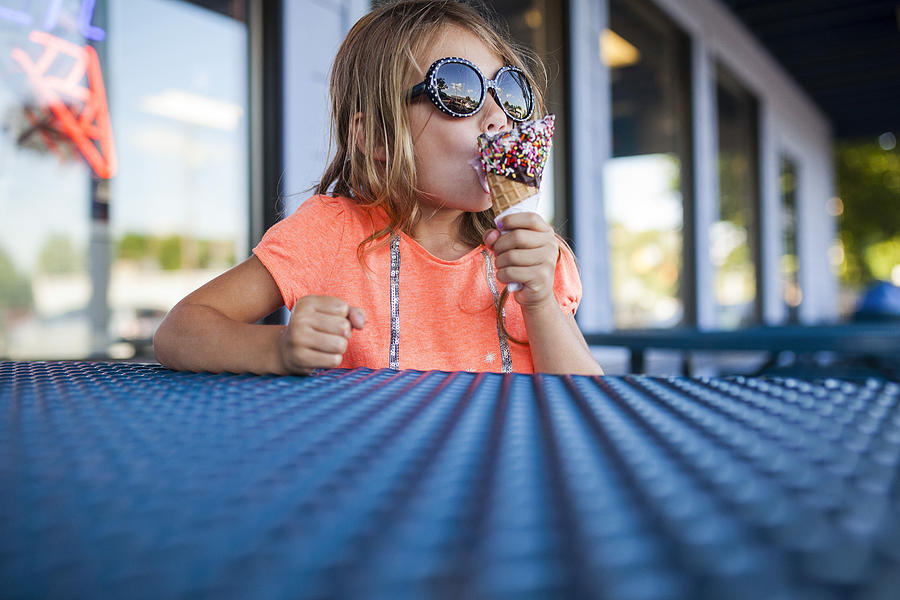 Girl in sunglasses eating ice cream at ice cream parlor Photograph by Cavan Images