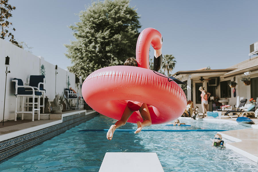 Girl jumping into swimming pool with pink flamingo Photograph by Cavan Images