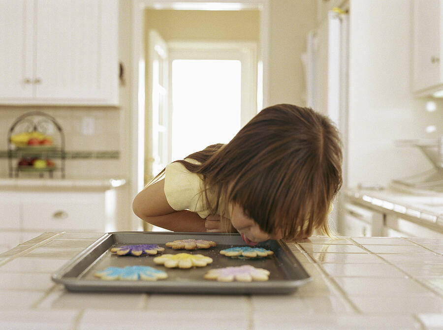 Girl leaning close to cookie sheet Photograph by Jupiterimages