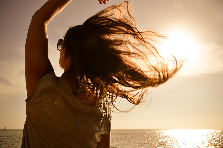 Girl looking the sea w/ hair in the wind at sunset Photograph by Volanthevist