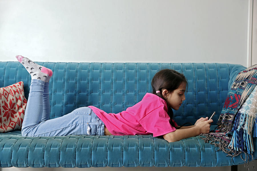 Girl lying on velvet sofa using mobile phone Photograph by Nick David