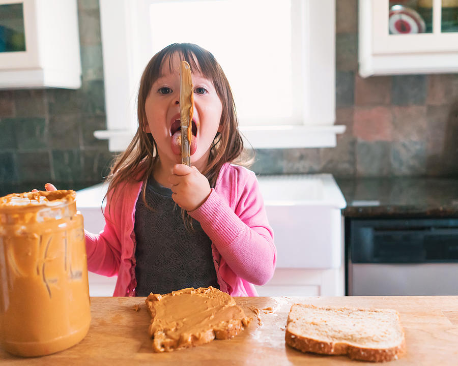 Girl making a peanut butter sandwich, licking the knife Photograph by Elizabethsalleebauer