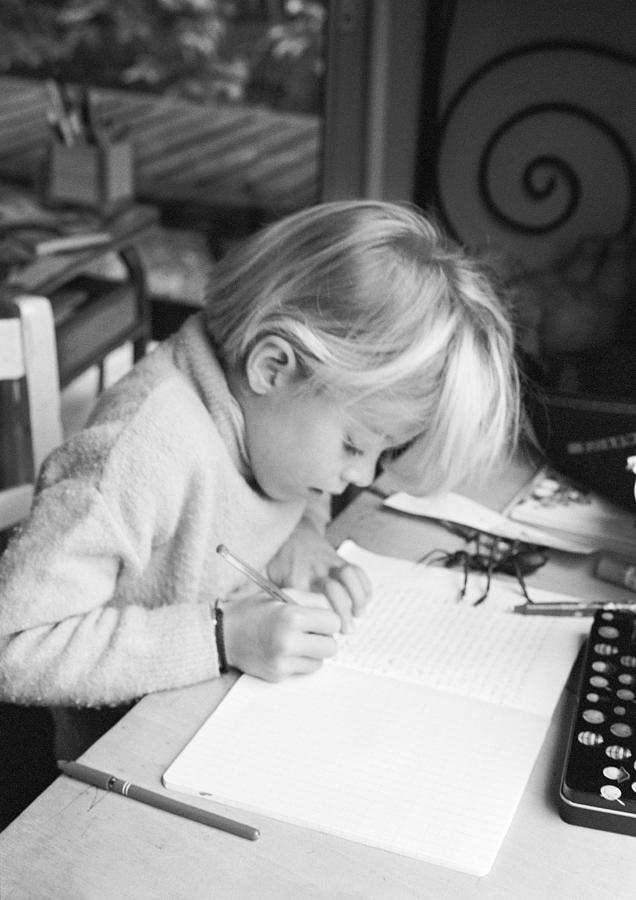Girl sitting at desk, writing in notebook, b&w Photograph by Laurence Mouton
