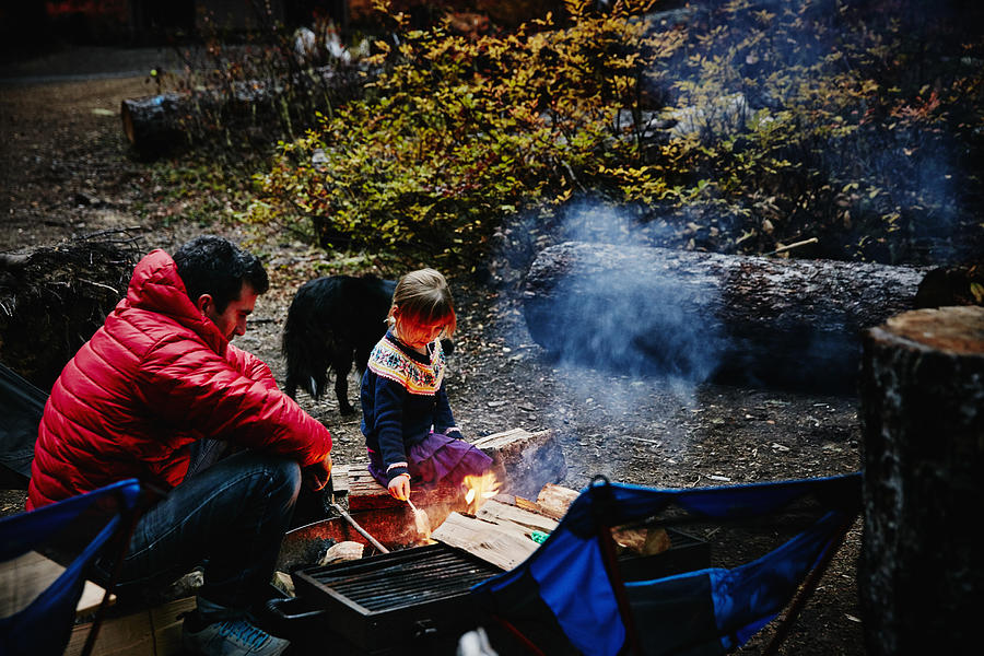 Girl sitting with father near fire while camping Photograph by Thomas Barwick