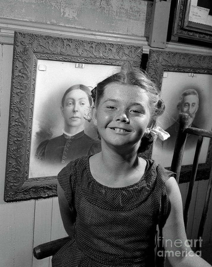 Girl standing in front of portraits of family members, 1946. Photograph by The Harrington Collection