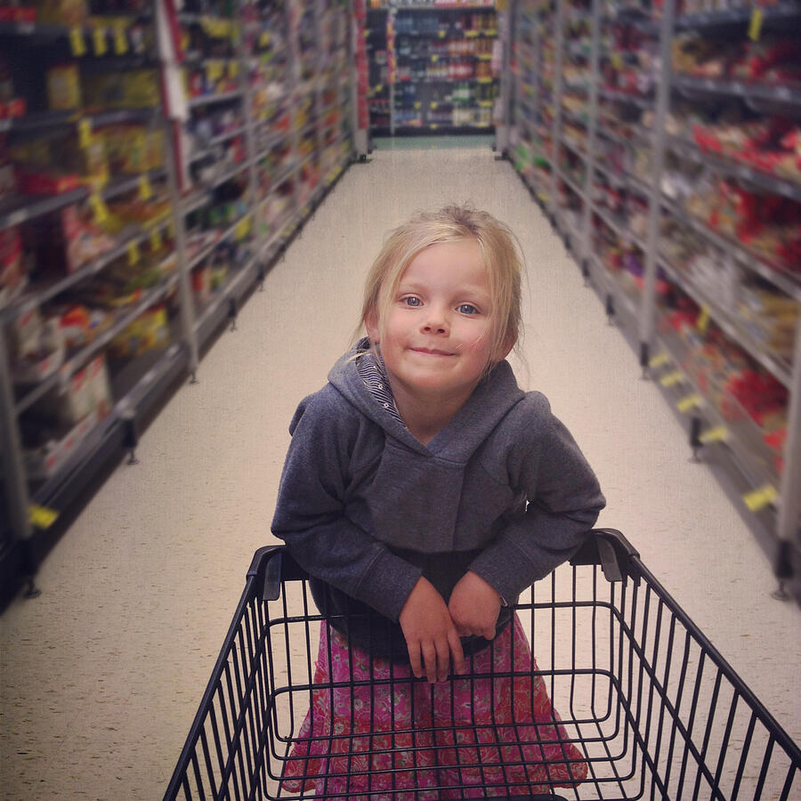 Girl standing on end of shopping trolley Photograph by Jodie Griggs